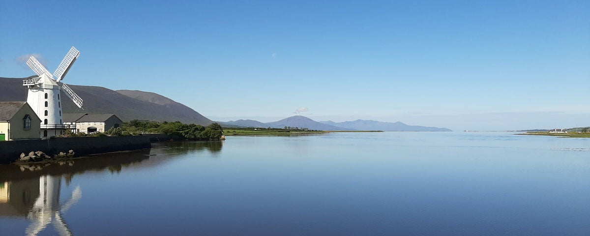 View of Blennerville Windmill overlooking the still waters of the harbour with mountains in the distance