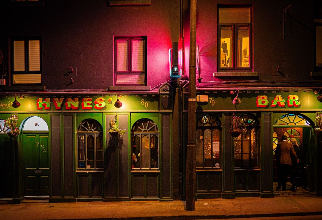 Exterior view of a bar illuminated at night with green frontage and traditional pub signage