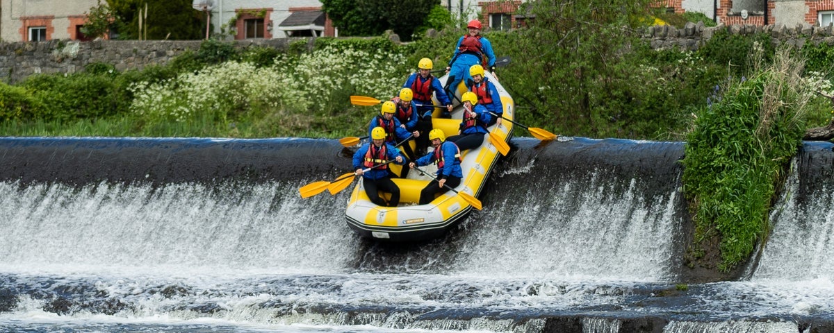 Eight people enjoying themselves rafting over a weir in a single raft