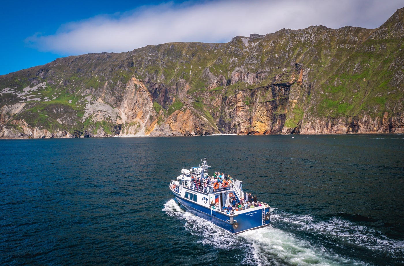 A boat with passengers heading towards high sea cliffs