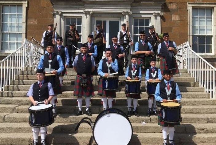 A group of people with drums dressed in blue kilts standing scattered around a flight of stone steps in front of a building