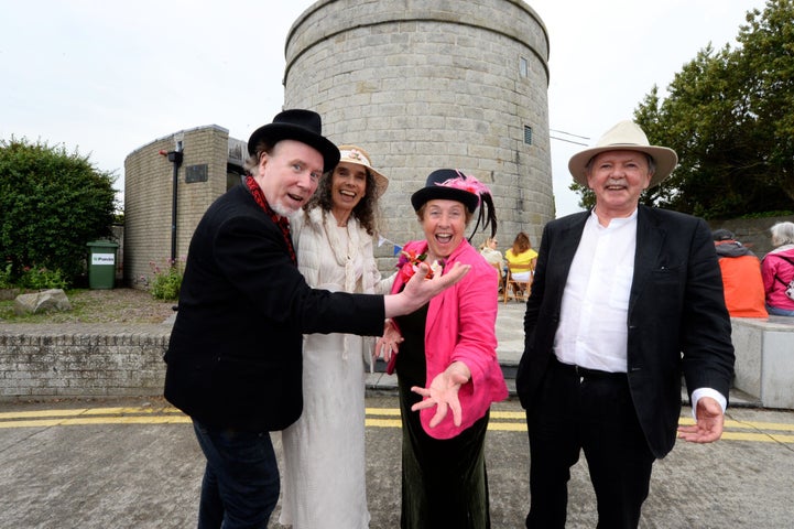 4 people in smart clothes standing in front of a round tower.