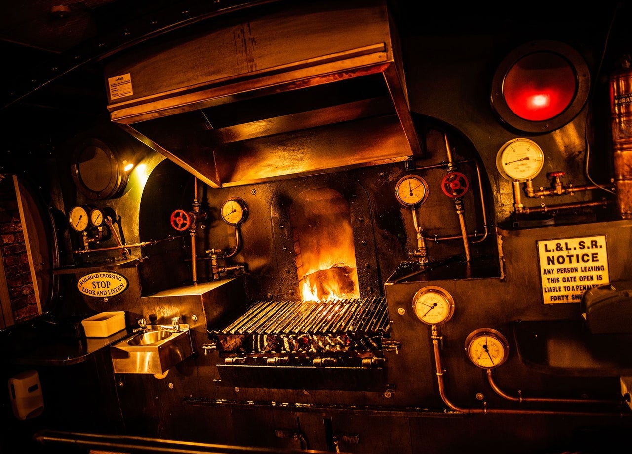 A firebox style grill glowing with open flames surrounded by vintage railway signage