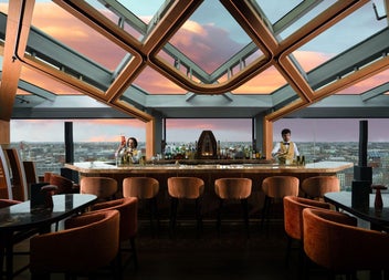 A rooftop bar interior and servers with panoramic views stretching across the city skyline at sunset