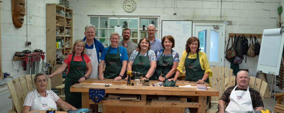 A group of people posing for a picture in aprons in front of a woodworking bench