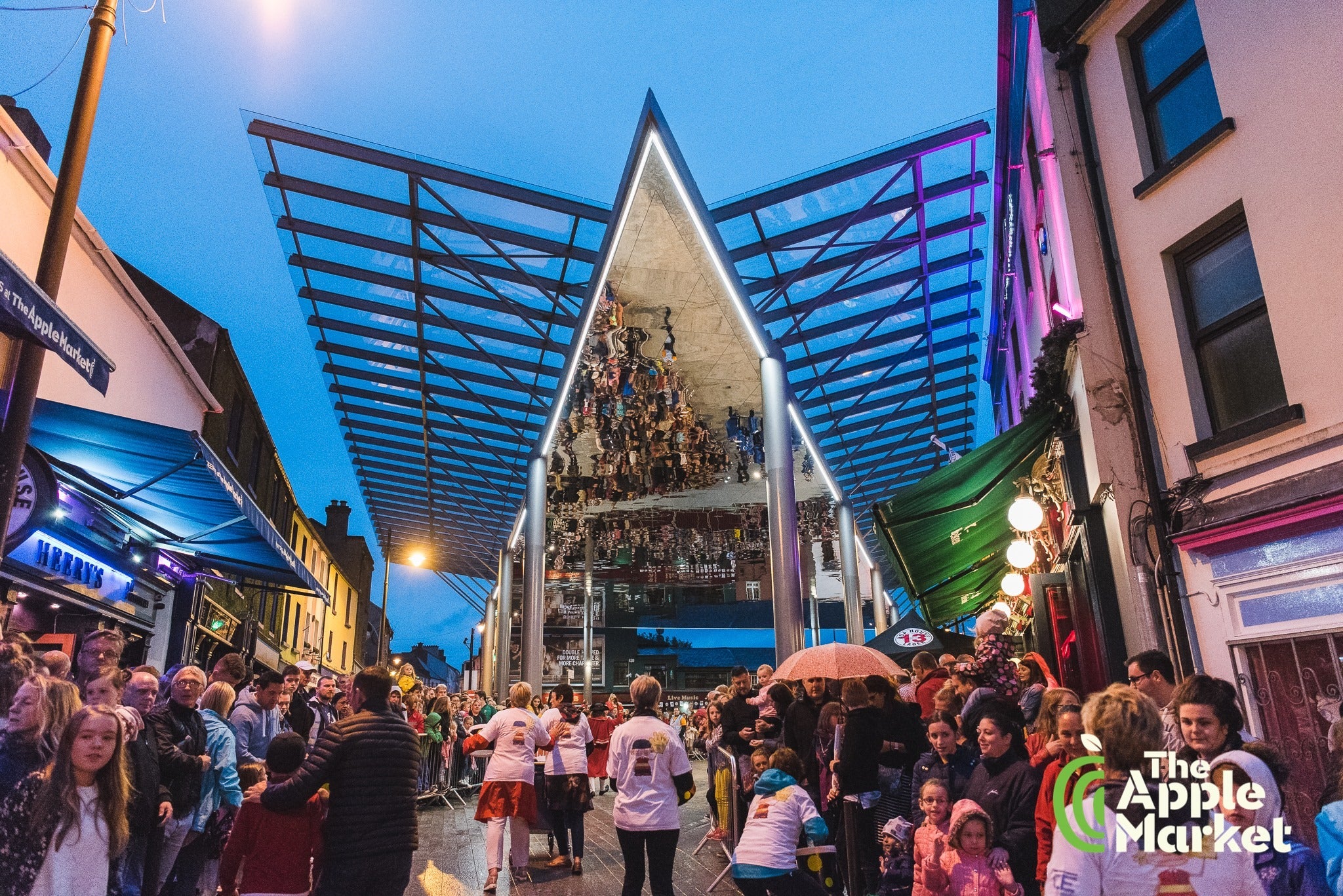 The Apple Market Sessions, outdoor area with large reflective canopy with crowds of people standing around.