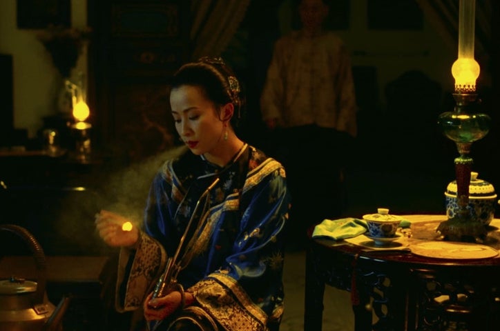 A Chinese woman is a well-made gown is sitting alone at a table. Her posture suggests sadness.