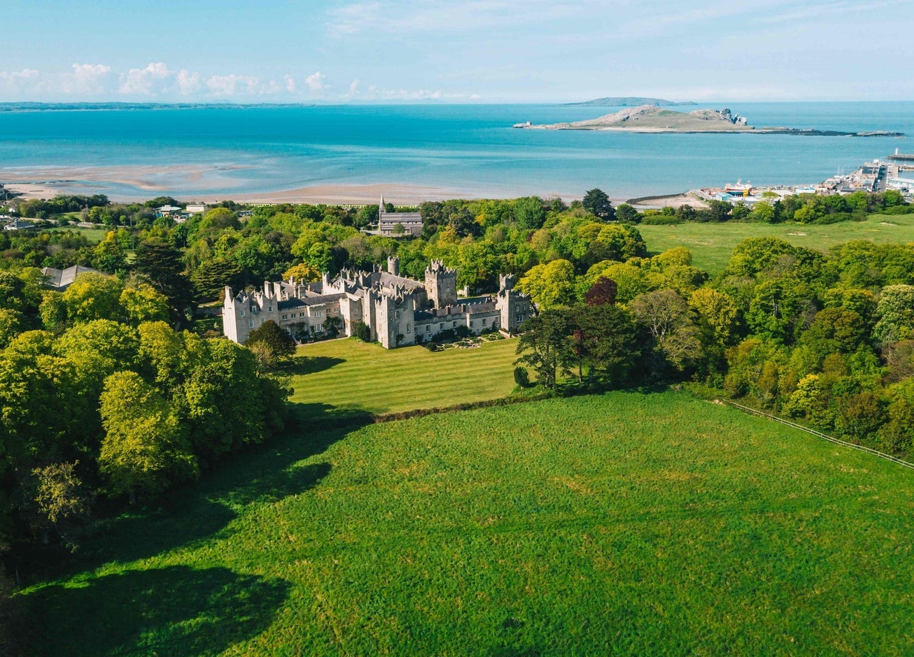 Aerial view of castle with green fields and coastal background