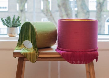 Two colourful fringed lampshades on a bench by a bright window