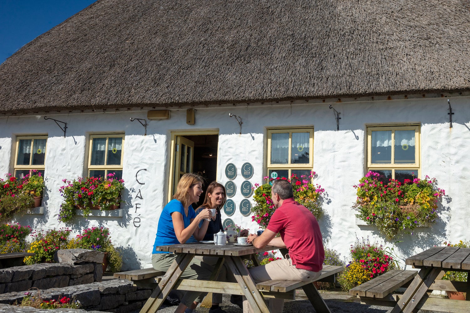 Three people sitting on a picnic table outside of Teach nan Phaidí in County Galway.