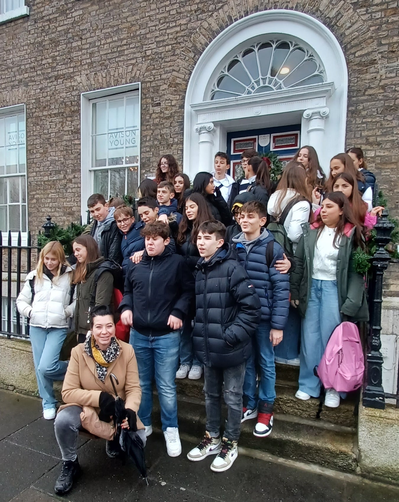 Group of teenagers and a tour guide posed on the steps of a Georgian house