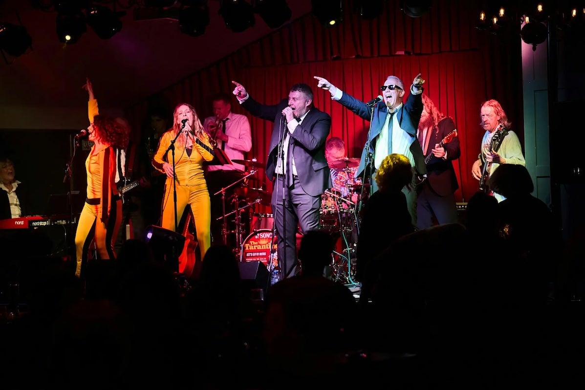 A group of 11 men and women singing and playing instruments with passion on a small stage.