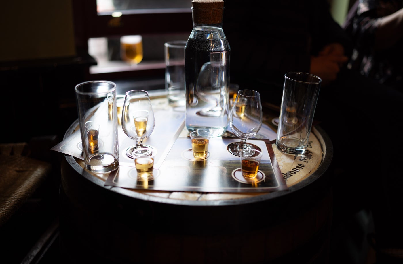 A bottle of whiskey and glasses sitting on a wooden whiskey barrel acting as a table