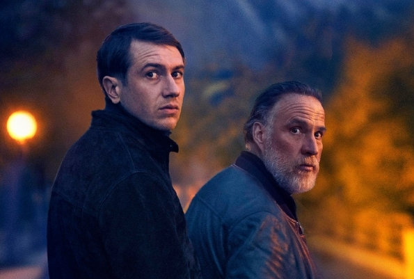 2 men in coats outside at night looking back over their right shoulders at the camera.