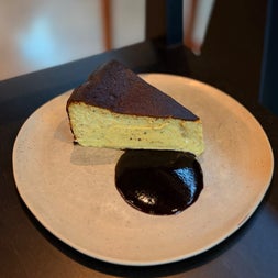 A slice of baked cheesecake on a ceramic plate with a dark chocolate sauce
