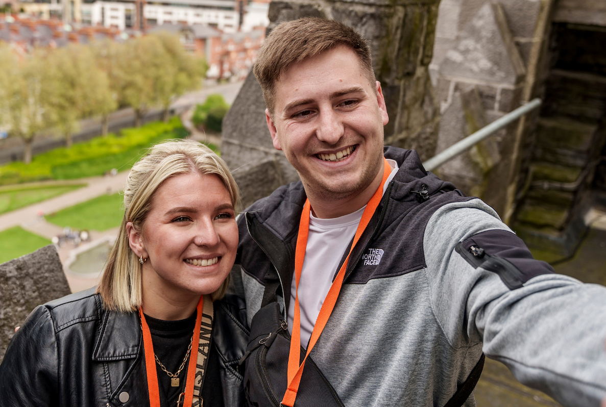 First Fortnight in partnership with St Patrick's Cathedral, 2 smiling people taking a selfie up high in stone building with blurry view of city below