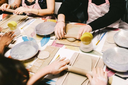 Looking down at table with hands rolling slabs of clay