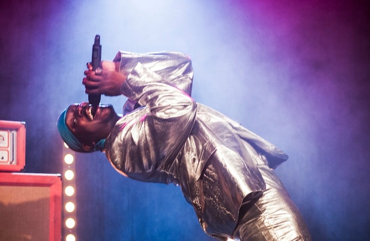 A man in shiny suit is singing into a hand held mic, bending backwards.