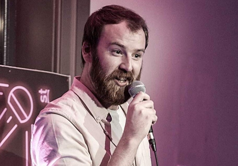 A man with a beard is talking into a mic he his holding.