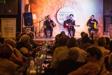 Three traditional musicians perform on a stage in front of an audience