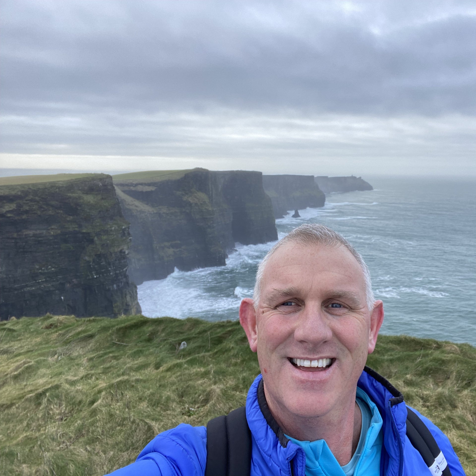 Selfie of a man in a blue jacket with cliffs and the sea in the background