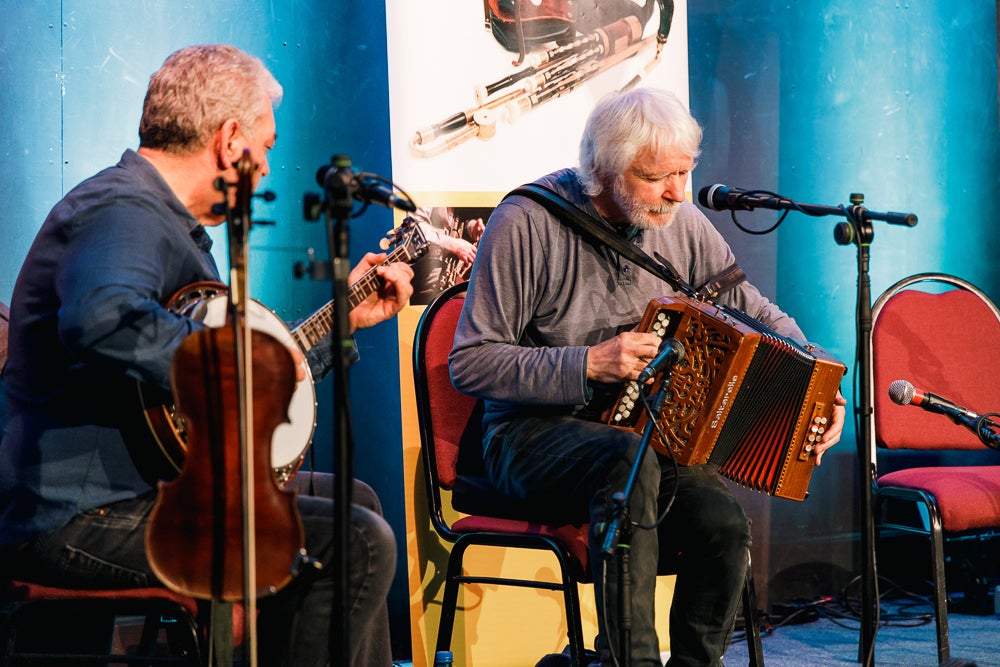 2 seated musicians playing on a small stage.