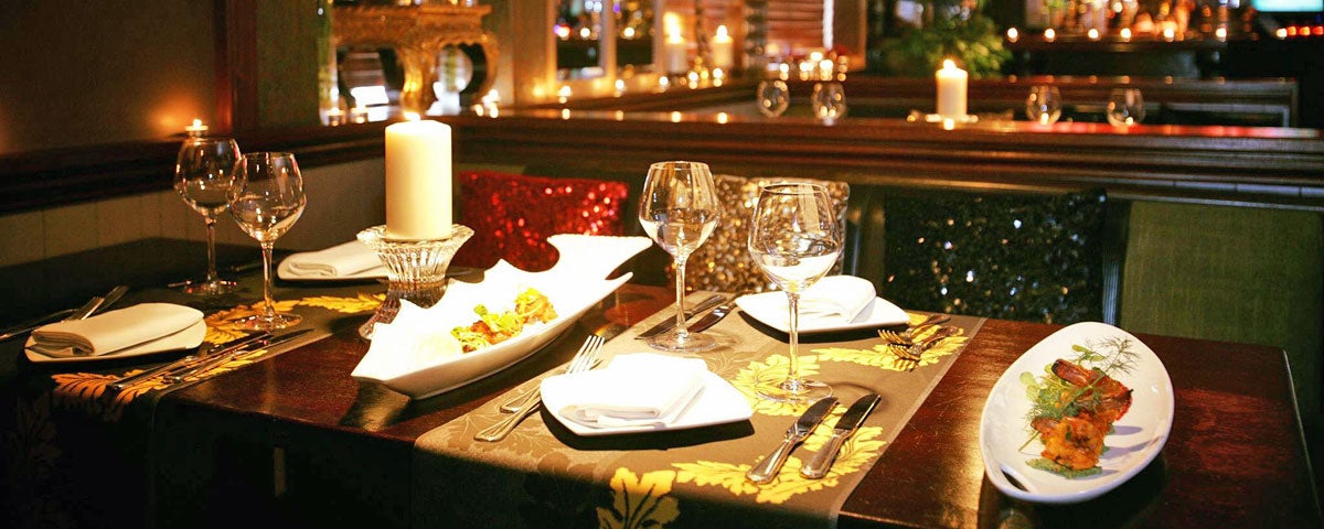 A table set for four in an Indian restaurant with a lit candle on the table and starter dishes to the side