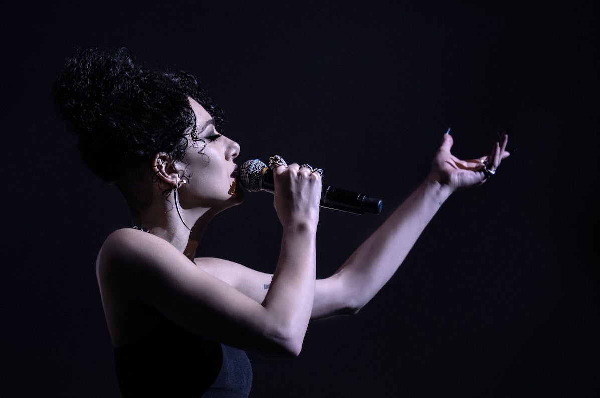 Noami Banks, vocalist - side view of woman singing into hand held mic with arm outstretched