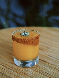 Shot glass with an orange coloured drink and spices along the edge