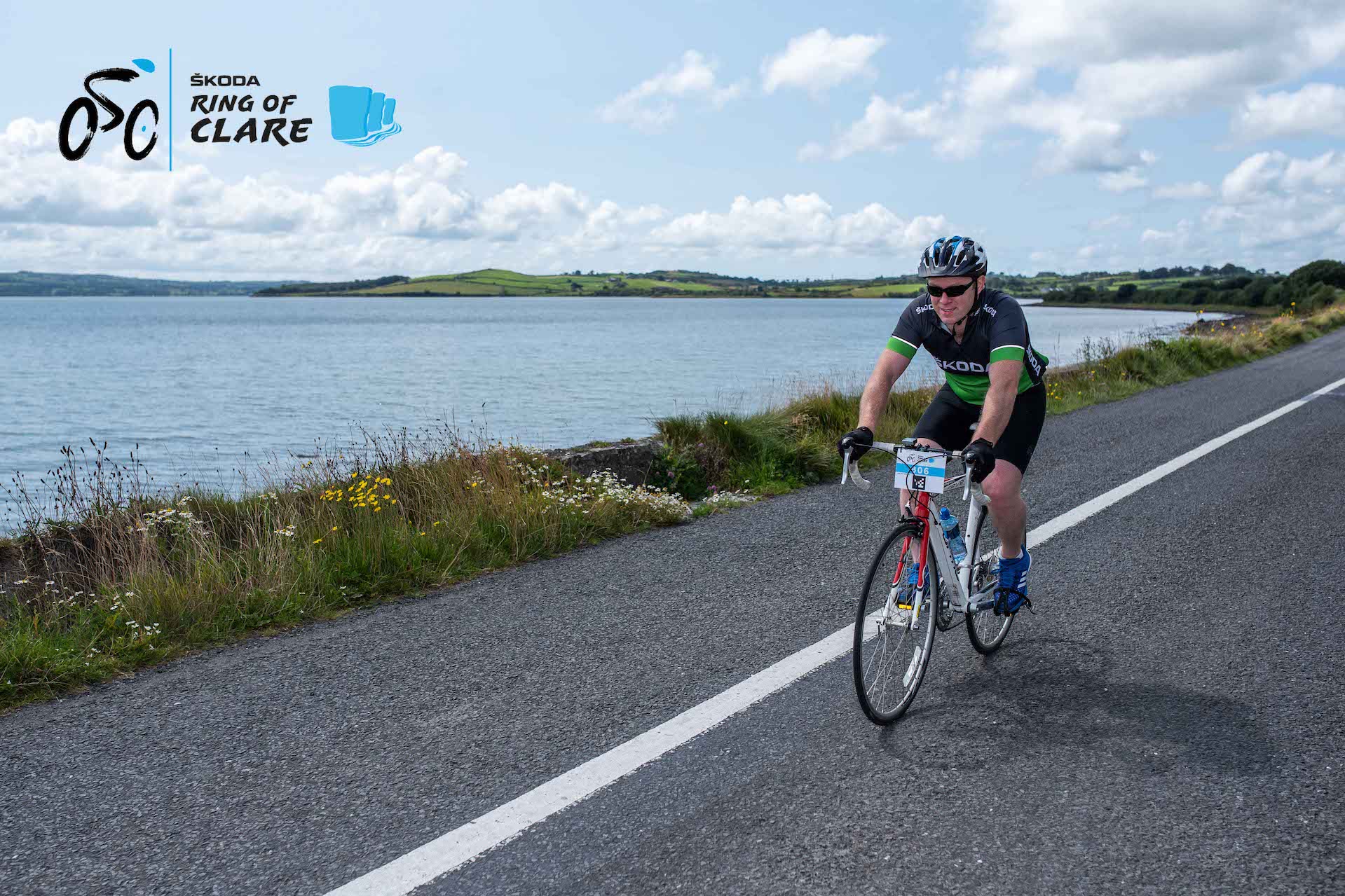 A cyclist of a road along side a way body of open water with hills in the distance.