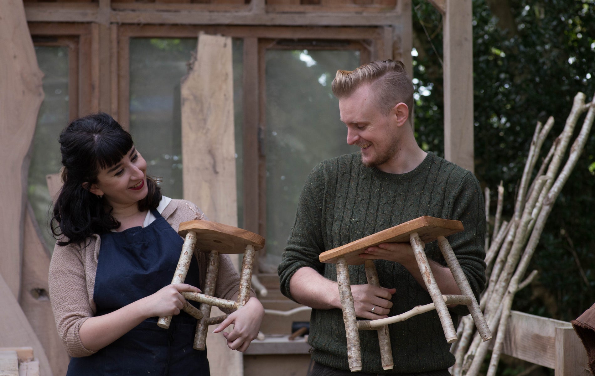 Two people holding wooden stools and smiling