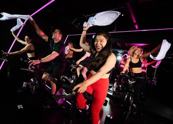 An spin class under neon lights with riders waving white towels