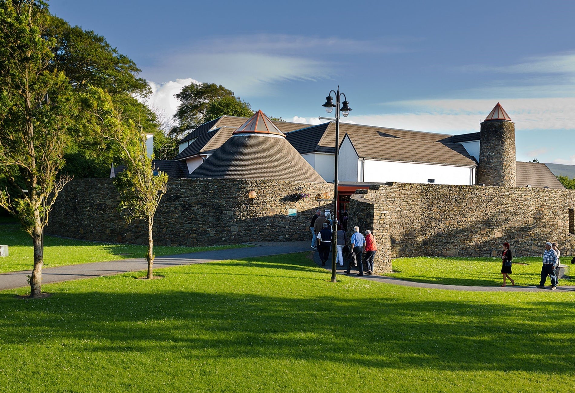 People walking through a park with trees into a building with a round stone wall