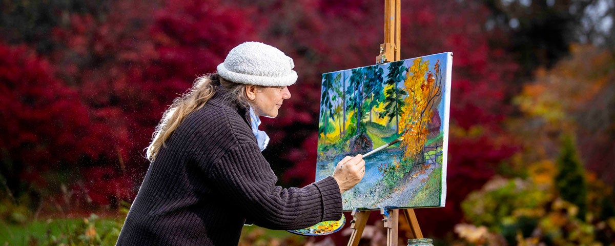 An artist outdoors at her easel painting a landscape
