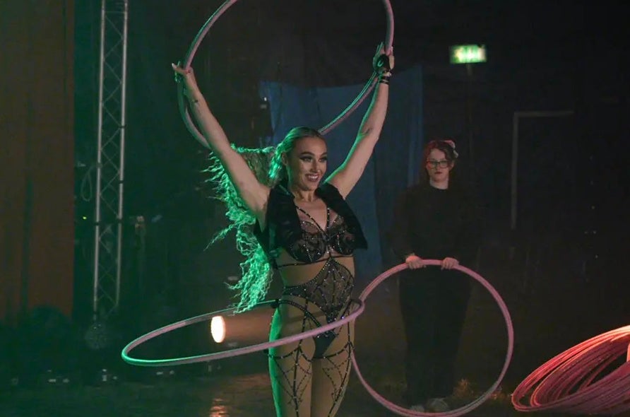 A smiling woman in a circus ring holding up hoola hoop