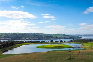 View of a golf course beside a water feature with the coast in the distance