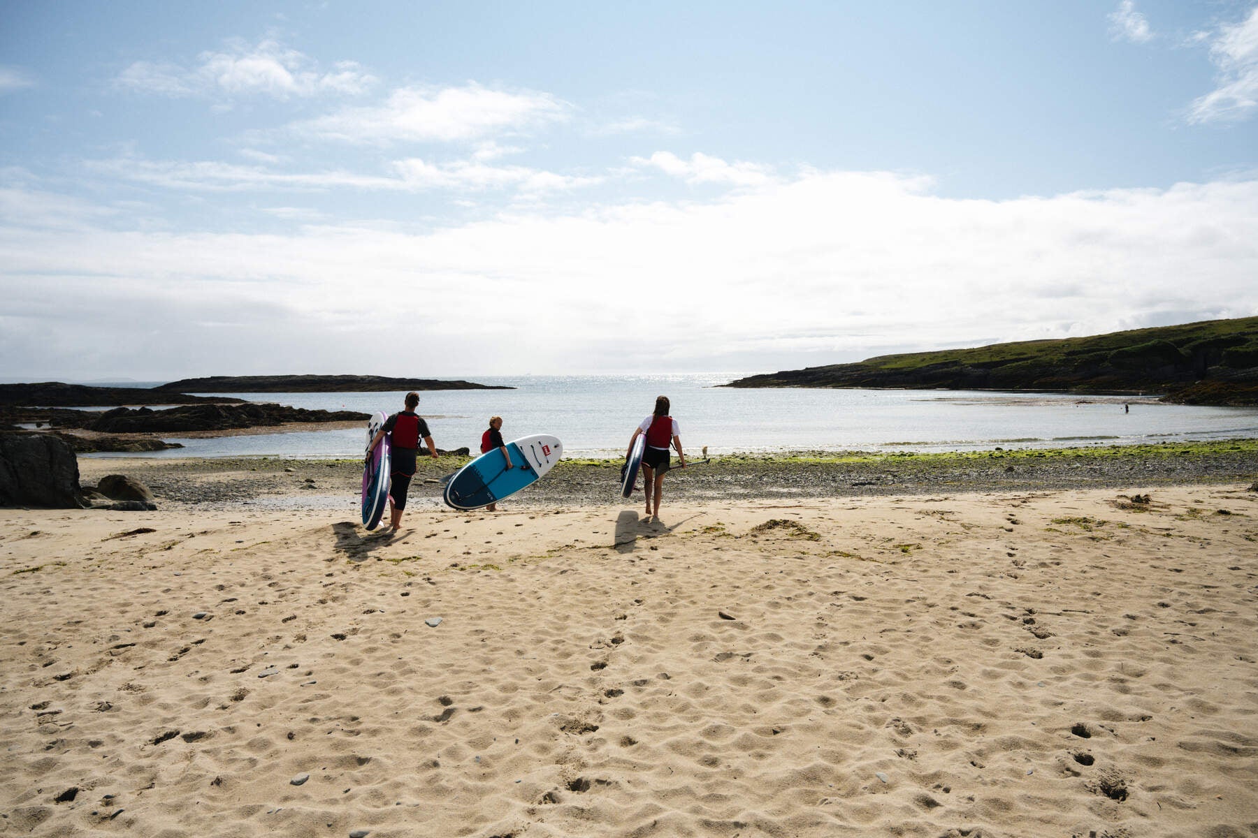 Three paddle boarders on the sand on their way into the sea