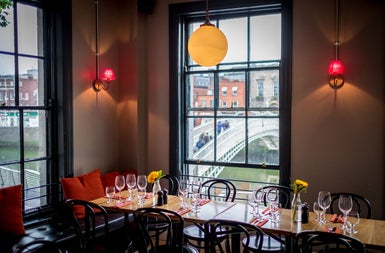 A restaurant with tables prepared for diners with old style windows and views of a bridge