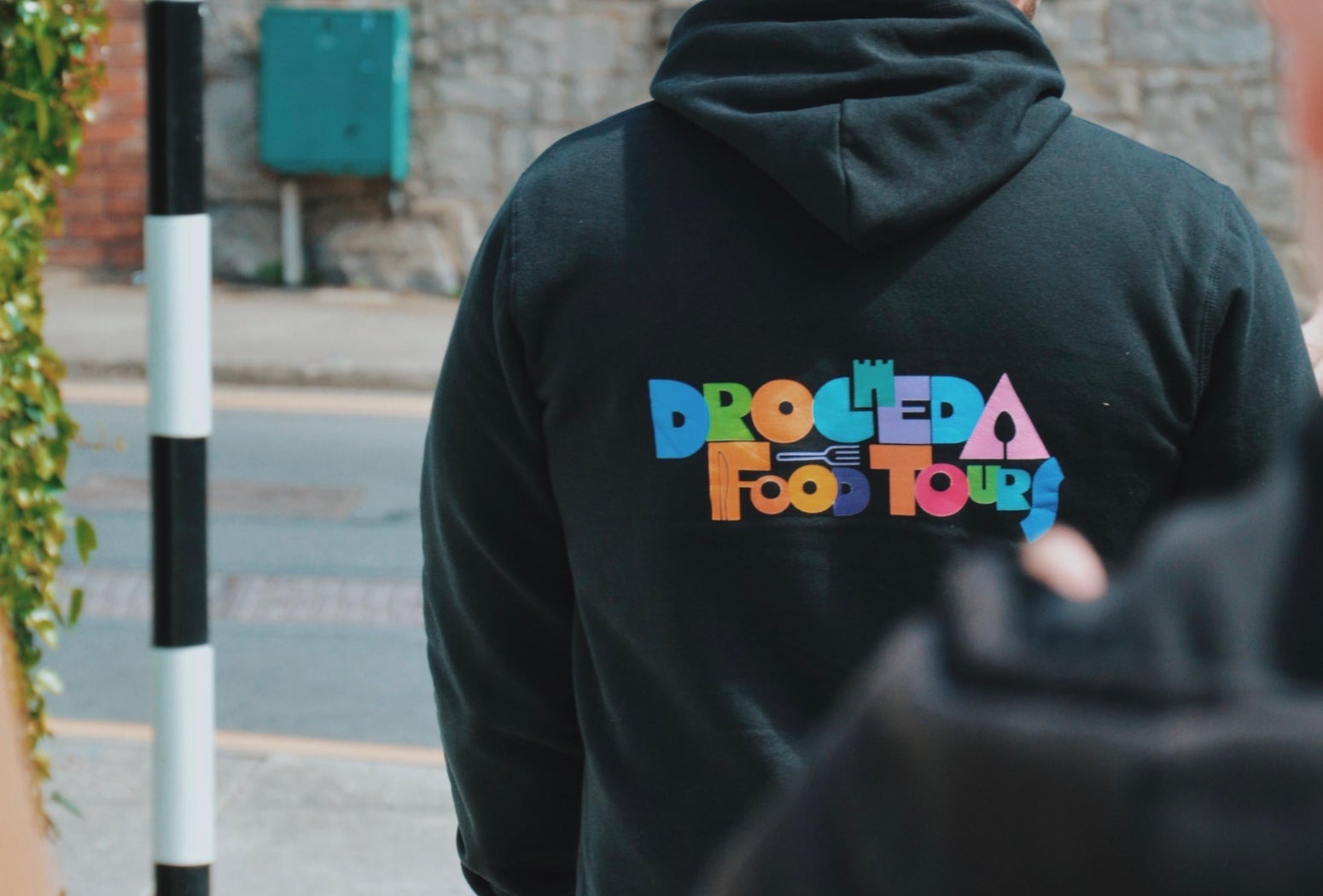 A person with their back to the camera wearing a hoodie with a Drogheda Food Tours logo