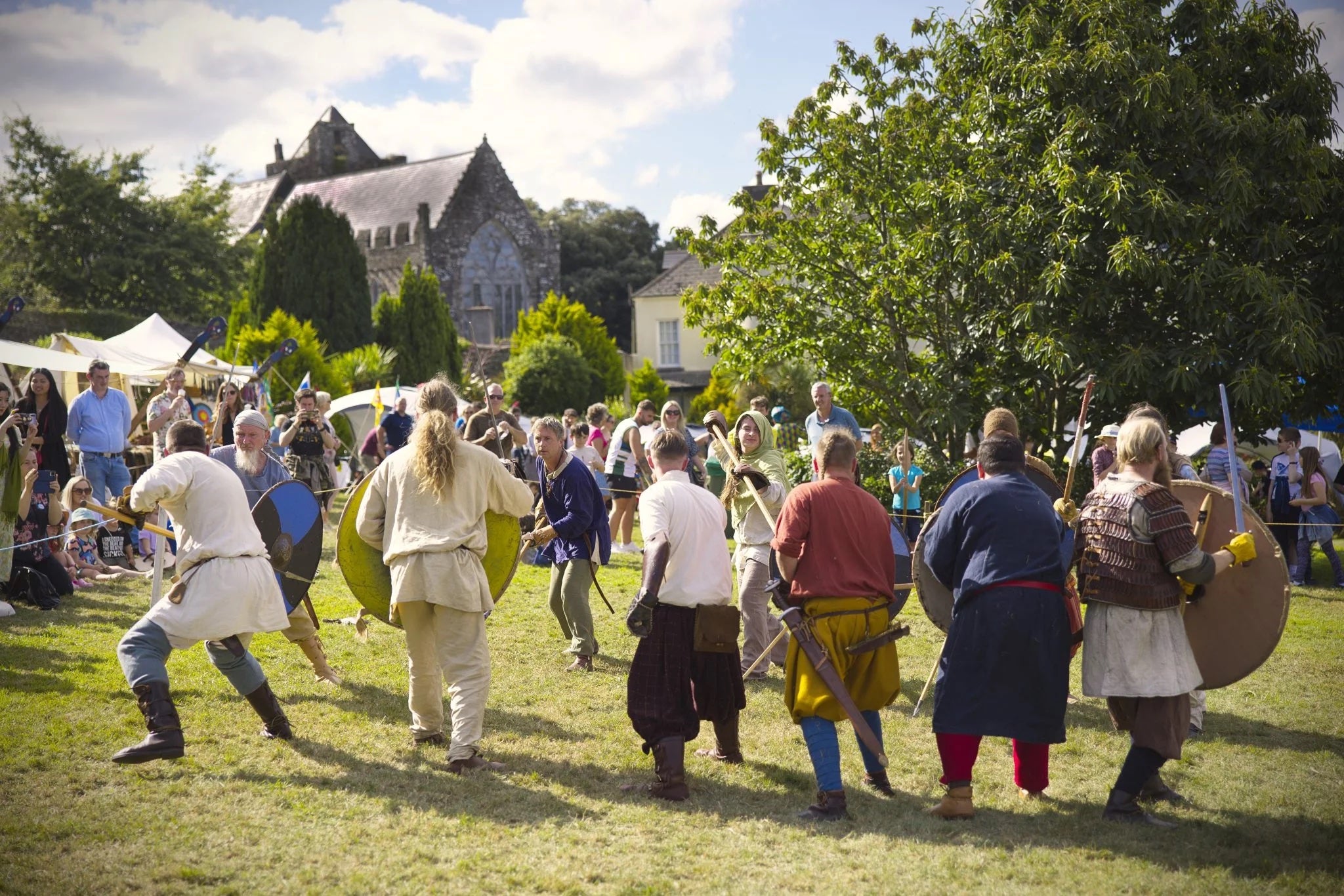 Men dressed in medieval clothes with weapons in mock battle watched by a crowd.