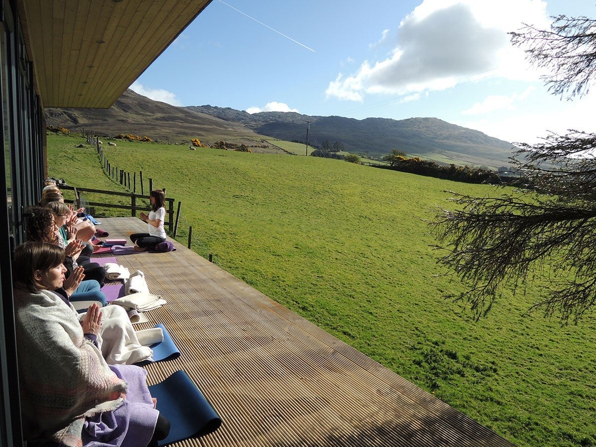 Group of people on sitting on yoga mats on a wooden decking facing a field