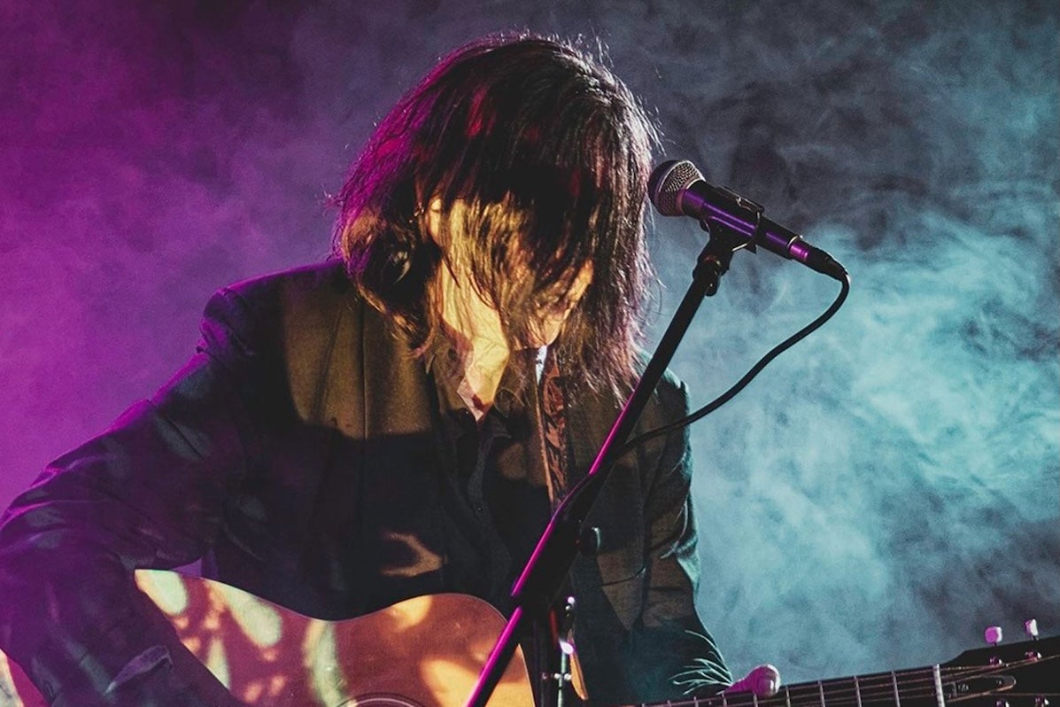 A man playing guitar with his face obscured by his long hair