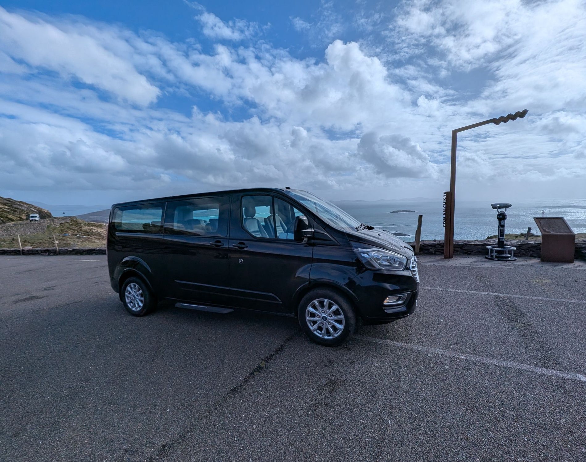 Black chauffeur minibus parked at a scenic coastal viewpoint