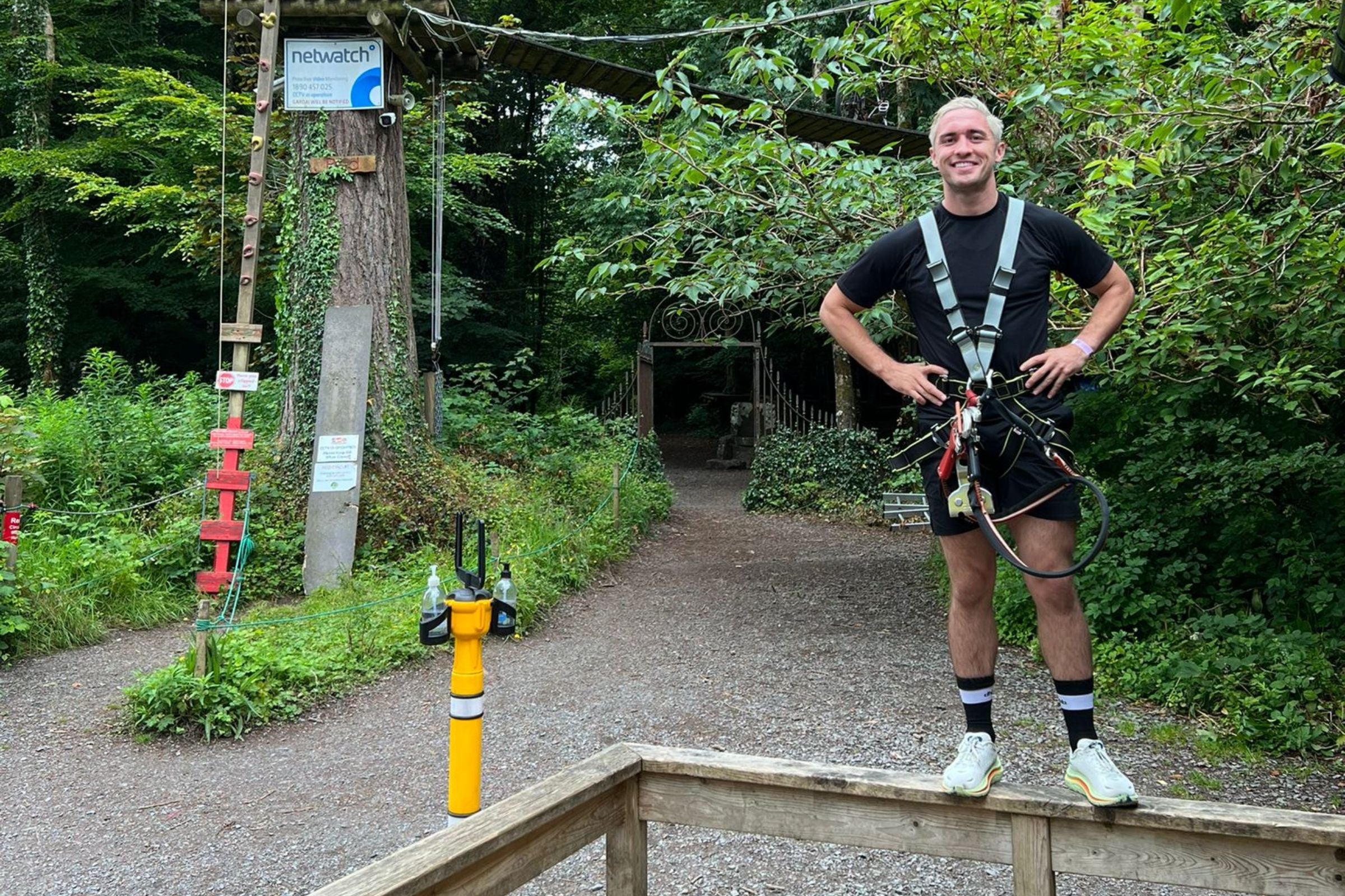 Man standing on a low fence in front of an adventure park.