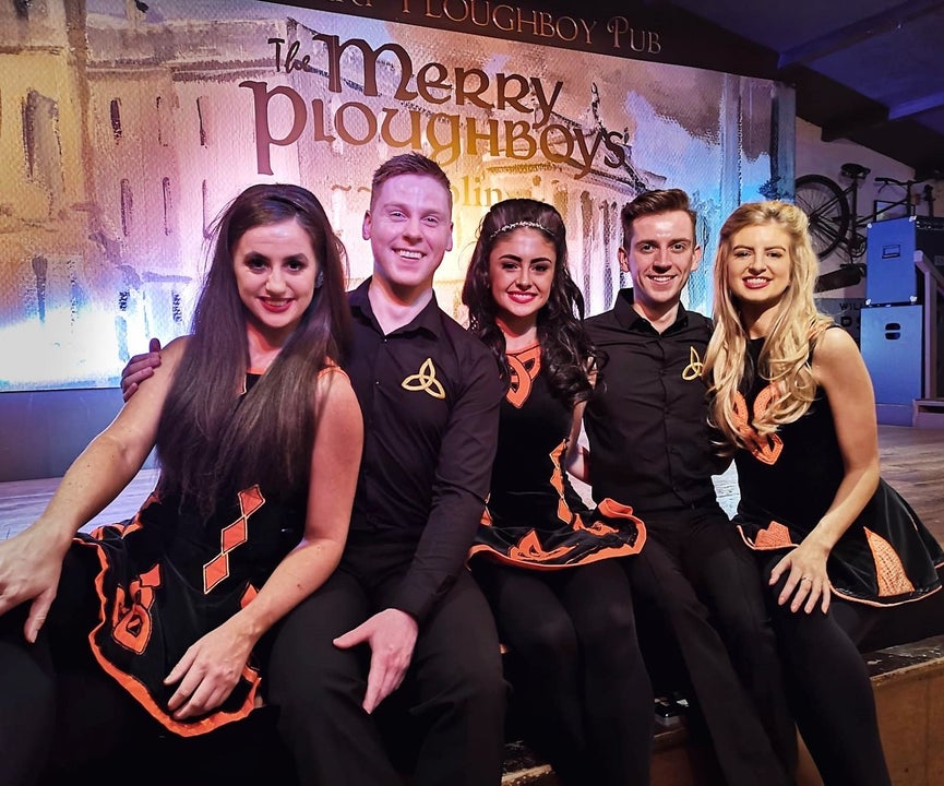 Five Irish dancers sit on a stage to pose for a photograph