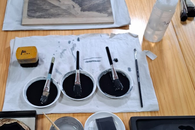 Japanese Water-Based Woodblock Printing (Mokuhanga), art materials for printing laid out on a table including pots of dark ink & brushes