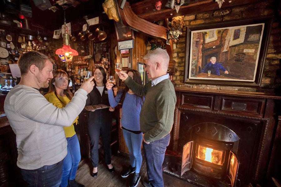 Four people tasting and toasting each other with whiskey by a pub fireside