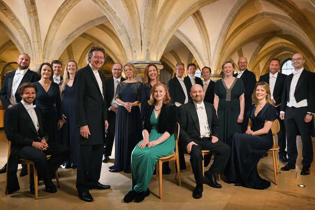 The Sixteen - A Choral Pilgrimage, a group of people in evening dress, some seated, under a low stone arched ceiling