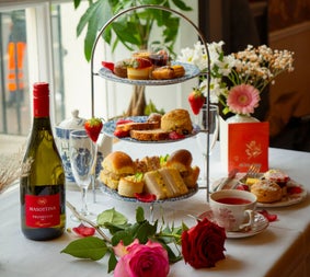 Afternoon tea stand with sandwiches cakes and scones served alongside tea prosecco and fresh flowers