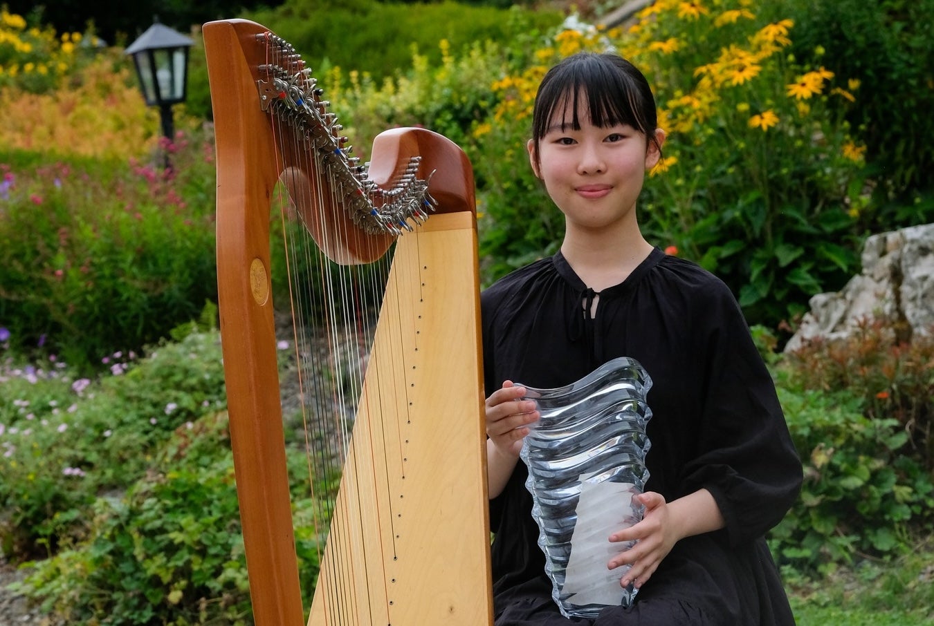 Winner of our International Harp Competition 2025, a smiling woman holding a glass trophy beside a harp.